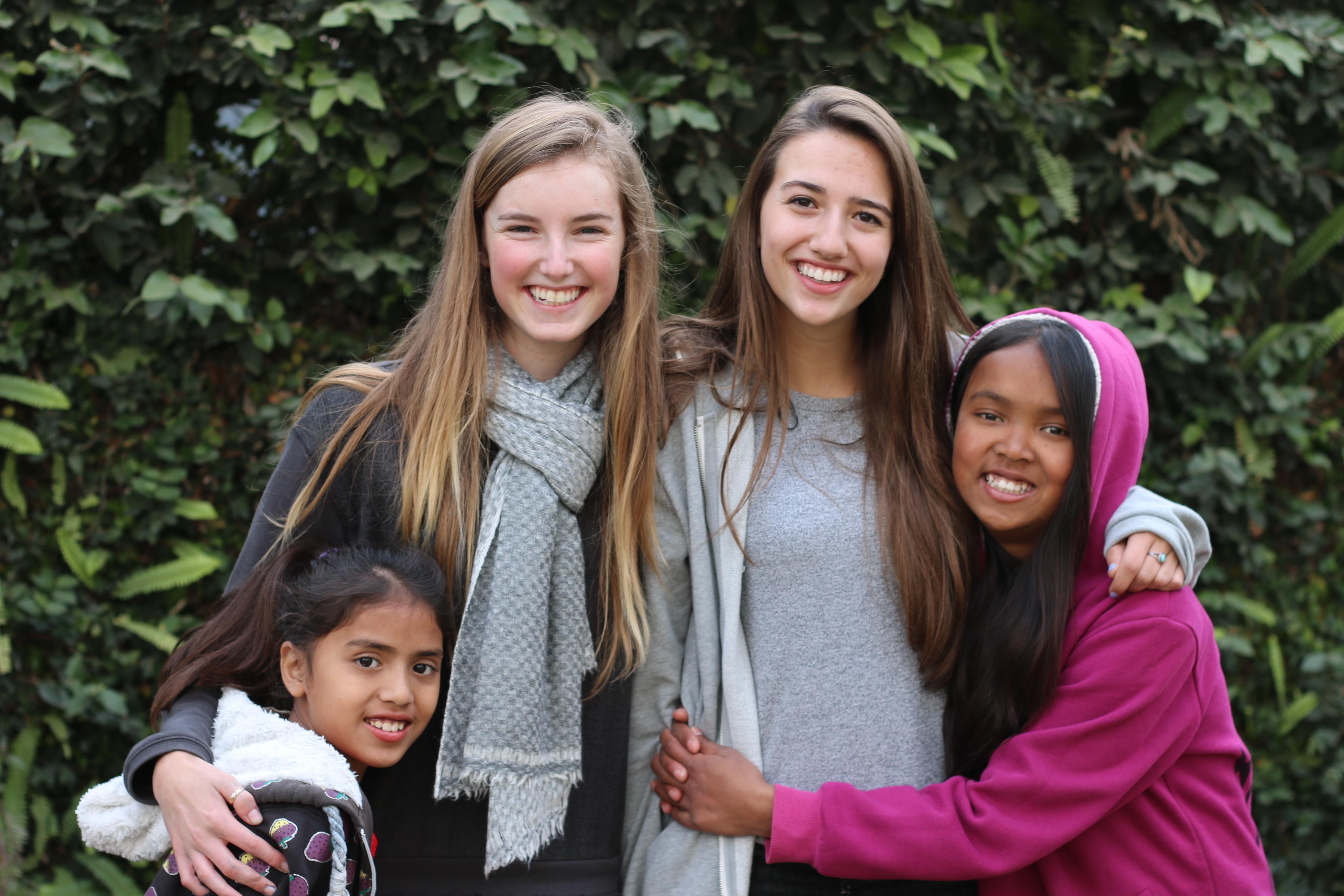 Two teenage community volunteers working in Nepal, take a photo with two young students at their placement. Teenage volunteers doing work with children in Nepal, take a photo with their students.